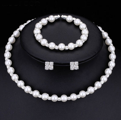 Bridal three-piece jewelry set with white pearls and clear rhinestones, including a necklace, bracelet, and square stud earrings.