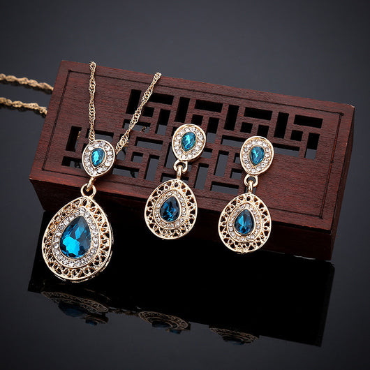 Gold-toned necklace and matching drop earrings set with blue teardrop crystals and clear rhinestones, on a wooden box. - Image 5