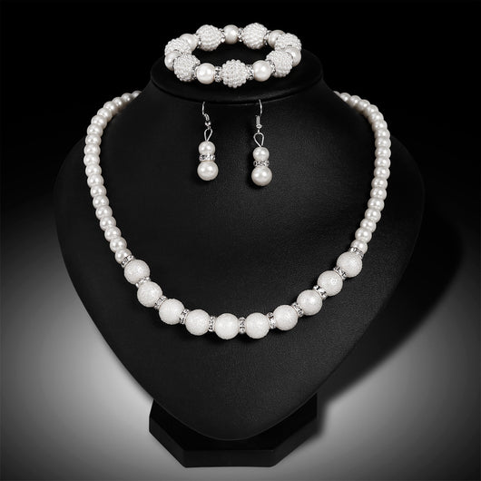 White faux pearl necklace, bracelet, and drop earrings set with rhinestone accents on a black display. - Image 6