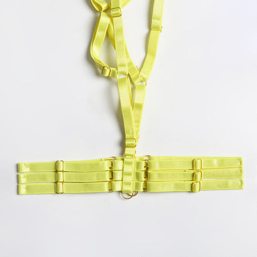 Woman in a neon yellow strappy harness lingerie set over a black lace bra and thong, sitting on a white bed. - Image 13