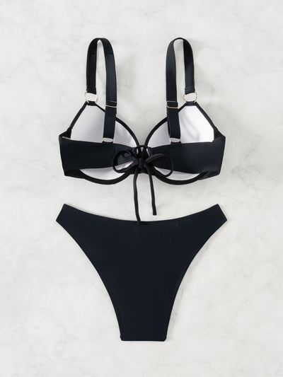Woman in a black pure color bikini with gold O-rings, featuring a push-up top and high-cut bottoms, by the ocean. - Image 5