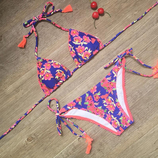 Women's blue floral print bikini with pink flowers, green leaves, coral trim, and orange tassels on ties.