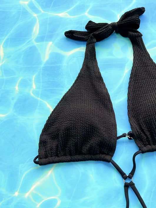 Woman in a black ribbed one-piece bikini with a halter neck and criss-cross tie details, posing against a textured wall. - Image 9