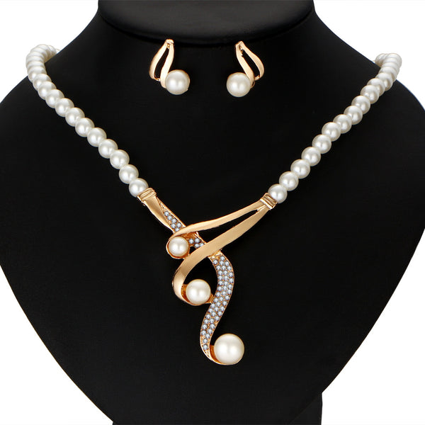 Gold-toned pearl clavicle necklace and matching stud earrings set with rhinestone accents on a black display.