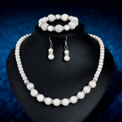 White faux pearl necklace, bracelet, and drop earrings set with rhinestone accents on a black display.