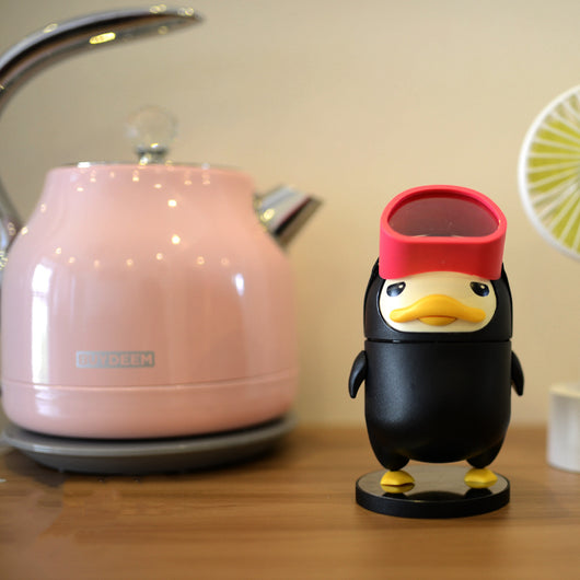 Black diving duck spray humidifier with red goggles and yellow feet, standing on a dark base on a table. - Image 9