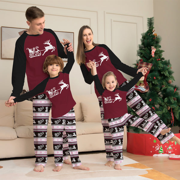 Child wearing a Christmas pajama set with a maroon and black reindeer top and black, pink, and white striped pants.