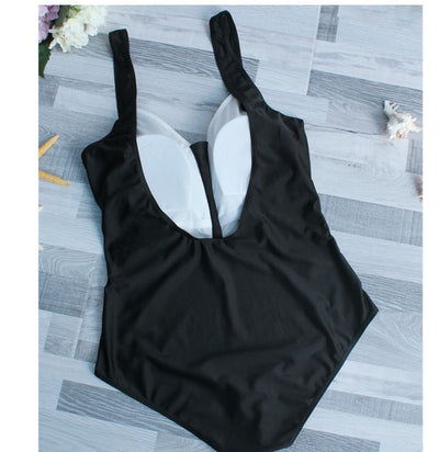 Woman in black one-piece swimsuit with white trim, wide-brimmed hat, and striped tote bag on a sunny beach. - Image 3