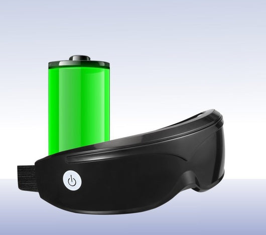 White and black eye massager with a goggle-like design, featuring a white frame and dark lenses, on a wooden surface. - Image 3