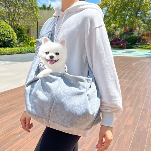 Person in white hoodie carrying a happy white dog in a navy blue pet sling bag outdoors. - Image 8