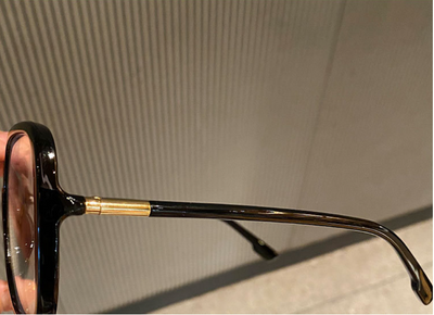 Black oversized square anti-blue light glasses with clear resin lenses and gold metal frame details, held by a hand. - Image 4