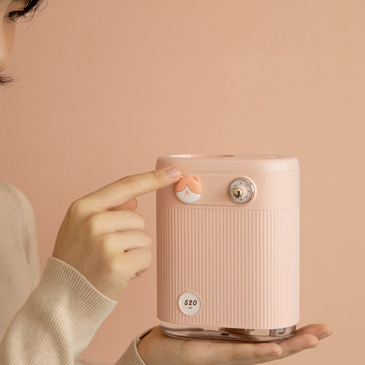 White cylindrical humidifier with ribbed texture, clear base, brown bear button, and silver dial, emitting mist on a white table. - Image 3