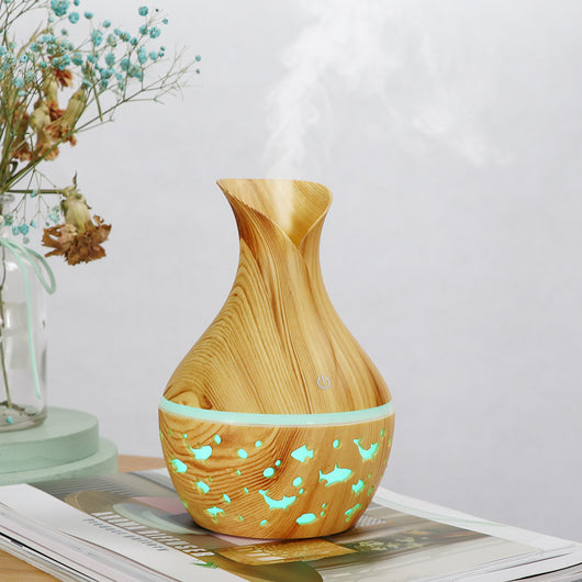 Dark wood grain humidifier shaped like a vase, with glowing green animal cutouts and mist emitting from the top.