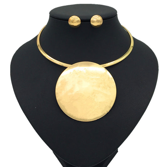 Silver-tone choker necklace with a large, flat circular pendant and matching round stud earrings on a black display.