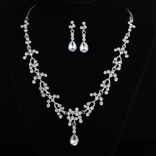 Silver-tone bridal jewelry set with a rhinestone floral necklace and matching teardrop dangle earrings on a black display.