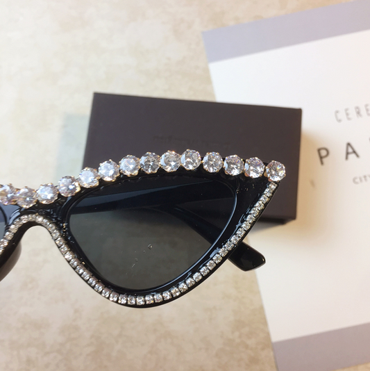 Two pairs of cat-eye sunglasses, one black with clear rhinestones and one pink with pink rhinestones, on a light surface. - Image 2