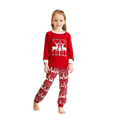 Family of four wearing matching red Christmas pajamas with white reindeer and tree patterns, standing by a decorated tree. - Image 7
