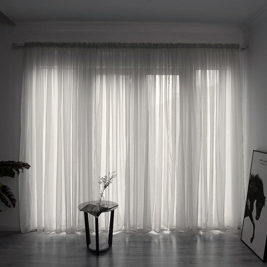 Simple and modern black sheer gauze curtain hanging on a rod in front of a window, filtering light.