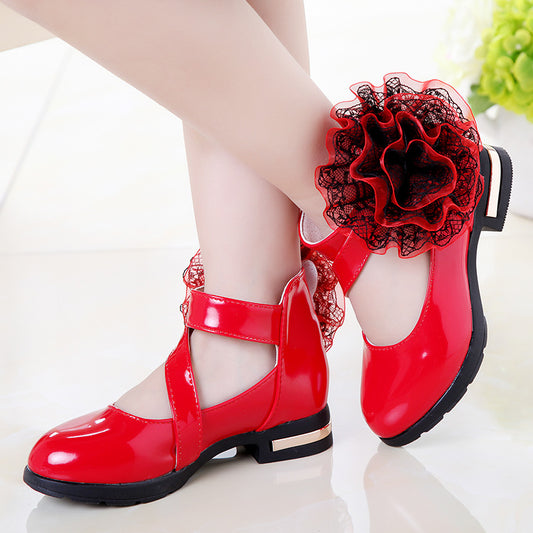 Shiny red princess shoes for little girls with a T-strap, Velcro closure, and a large red and black lace flower.