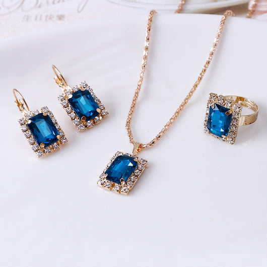 Gold-toned three-piece jewelry set with rectangular clear crystal necklace, matching drop earrings, and adjustable ring.