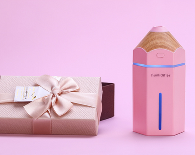 Light blue pencil-shaped mini humidifier with wood-grain top and glowing green light, next to a white teacup and pink gift box. - Image 4