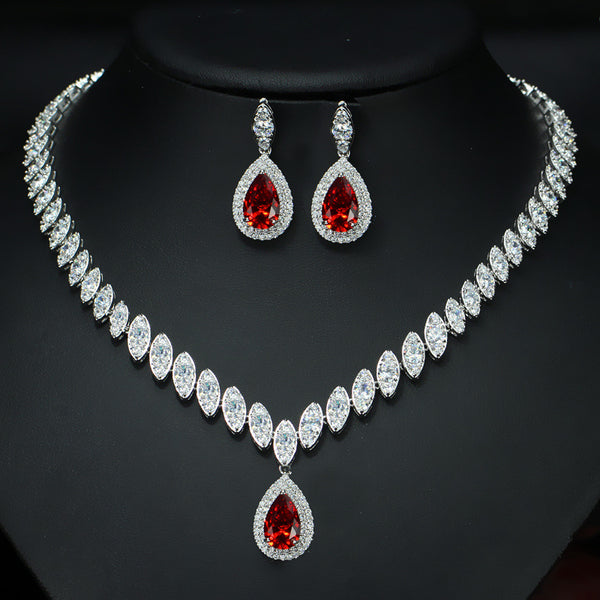 Silver-toned necklace and earring set with red teardrop stones and clear marquise-cut accents on a black display.
