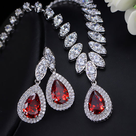 Silver-toned necklace and earring set with red teardrop stones and clear marquise-cut accents on a black display. - Image 2