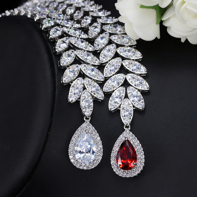 Silver-toned necklace and earring set with red teardrop stones and clear marquise-cut accents on a black display. - Image 3