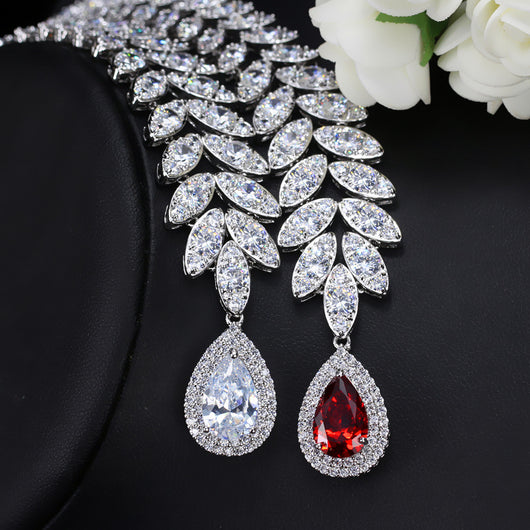 Silver-toned necklace and earring set with red teardrop stones and clear marquise-cut accents on a black display. - Image 3