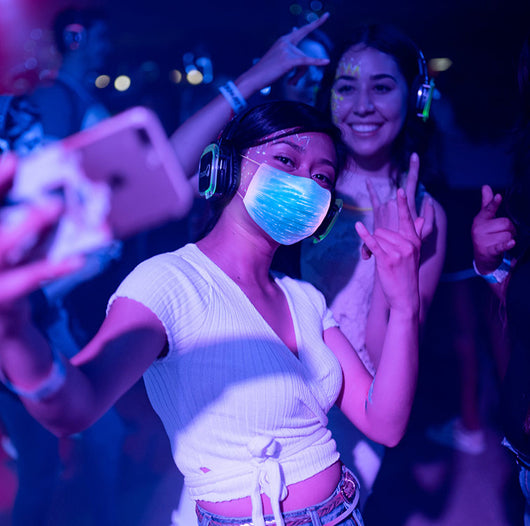 White LED mask with adjustable ear loops, a USB charging cable, and an instruction manual on a wooden surface. - Image 11