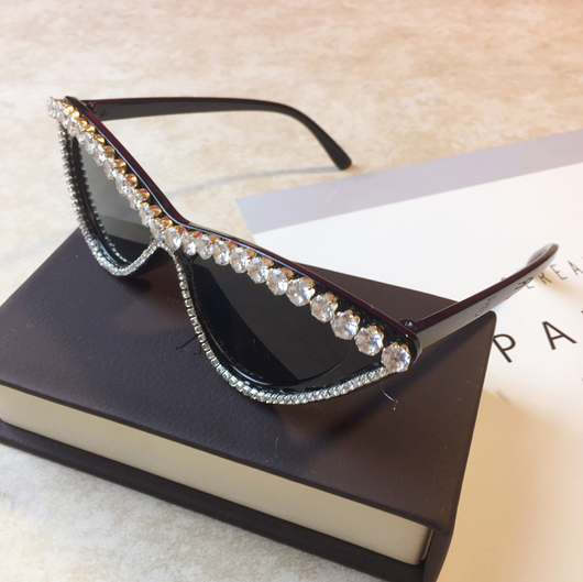Two pairs of cat-eye sunglasses, one black with clear rhinestones and one pink with pink rhinestones, on a light surface. - Image 3