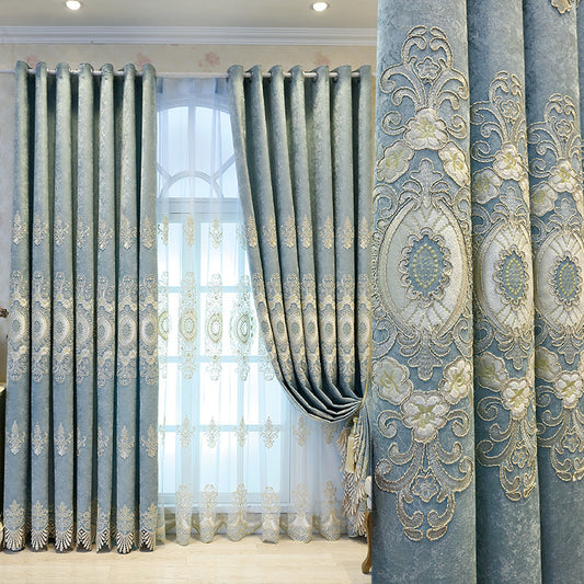 Blue sheer curtain with intricate gold and dark blue embroidery in a European classical style, draped over a window.