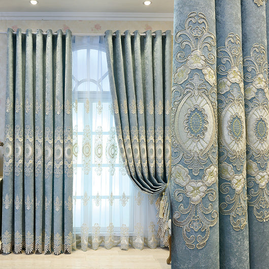 Blue sheer curtain with intricate gold and dark blue embroidery in a European classical style, draped over a window.