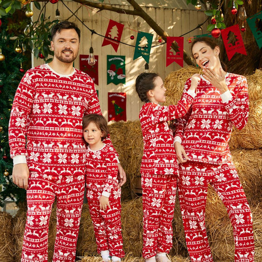 Family of four wearing matching red and white Christmas pajamas with reindeer and snowflake patterns, smiling.
