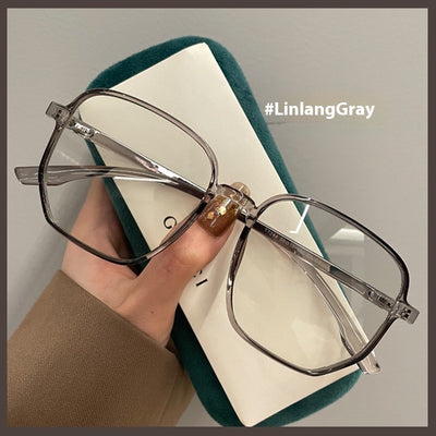 Mocha brown irregular frame glasses with clear lenses, held over a dark green velvet glasses case. - Image 7