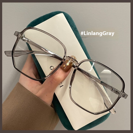 Mocha brown irregular frame glasses with clear lenses, held over a dark green velvet glasses case. - Image 7