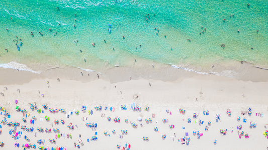 Aerial view of a vibrant summer beach with turquoise water, white sand, and colorful umbrellas.
