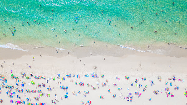 Aerial view of a vibrant summer beach with turquoise water, white sand, and colorful umbrellas.