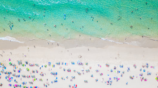 Aerial view of a vibrant summer beach with turquoise water, white sand, and colorful umbrellas.