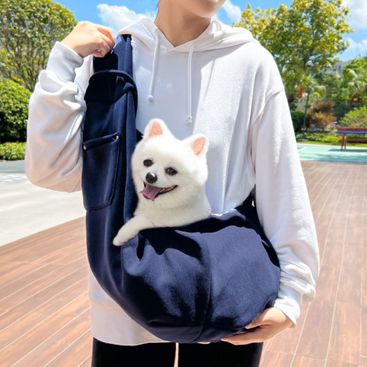 Person in white hoodie carrying a happy white dog in a navy blue pet sling bag outdoors. - Image 7