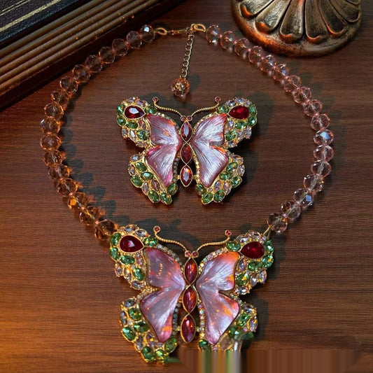 Pink enamel butterfly brooch with green, red, and clear rhinestones set in gold-toned metal.
