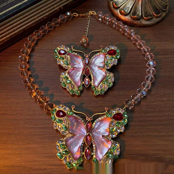 Pink enamel butterfly brooch with green, red, and clear rhinestones set in gold-toned metal.