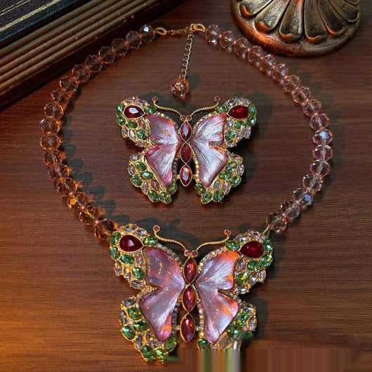 Pink enamel butterfly brooch with green, red, and clear rhinestones set in gold-toned metal.
