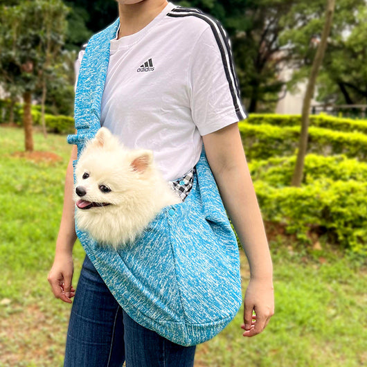 Person in white hoodie carrying a happy white dog in a navy blue pet sling bag outdoors. - Image 32
