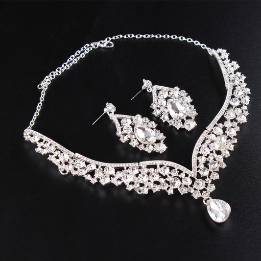 Sparkling silver-tone necklace and matching earrings set with clear round and teardrop rhinestones on a black display.