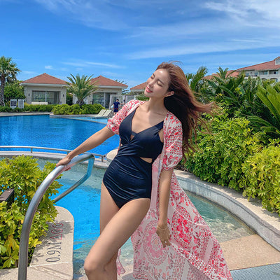 Woman in black one-piece swimsuit with side cutouts and a pink floral kimono cover-up by a resort pool. - Image 6