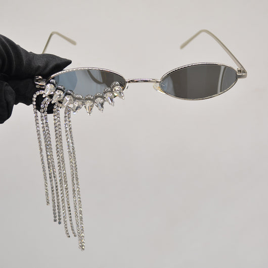 Silver oval-frame sunglasses with mirrored lenses and glamorous rhinestone tassels on one side, held by a gloved hand. - Image 3