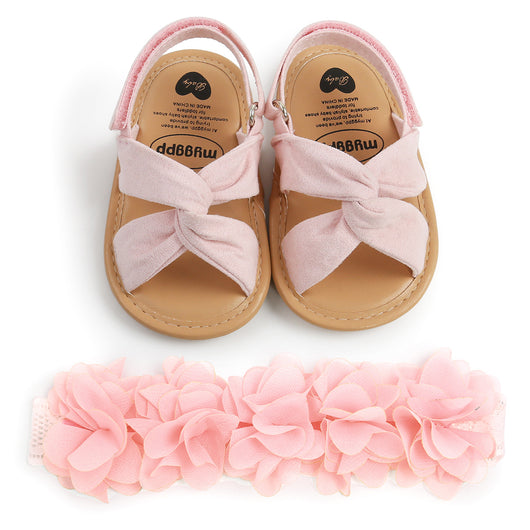 Black baby sandals with knotted cross straps and a matching black floral headband on a white background. - Image 13