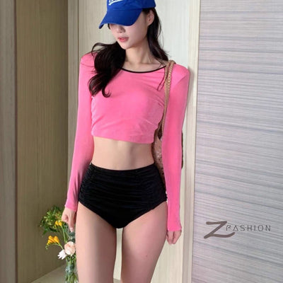 Woman in a pink long-sleeved crop top and black high-waisted ruched swim bottoms, posing in a mirror. - Image 3