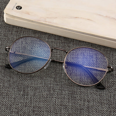 Gold round-frame anti-blue light glasses with clear resin lenses on a gray textured surface next to a notebook. - Image 13